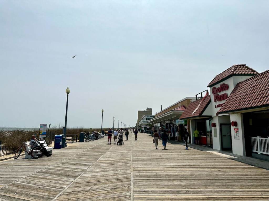 rehoboth-beach-boardwalk People walk down a boardwalk at Rehoboth Beach on a sunny day.
