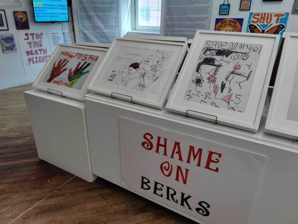 Drawings and other artworks are displayed in a showcase in the center of a room.