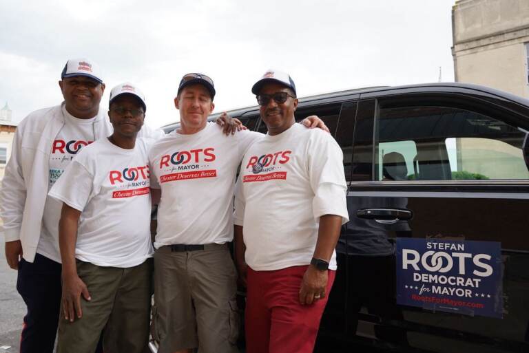 Stefan Roots poses with other people in front of a car.