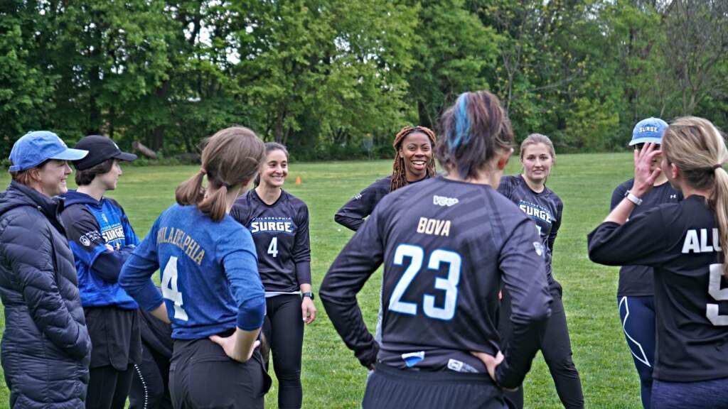 surgeultimatefrisbee-07-scaled A group of players are gathered in a circle, laughing and smiling.