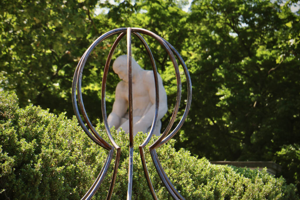 A sculpted figure of a man is visible through the bars of a steel sculpture in the foreground.