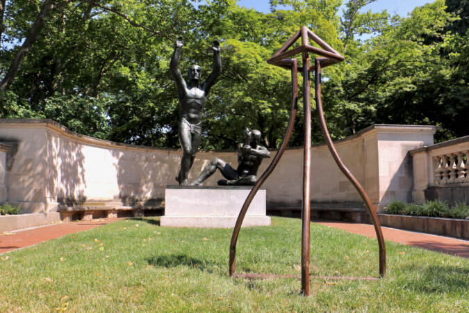 In the foreground, a steel sculpture. In the background, two sculpted figures are visible.