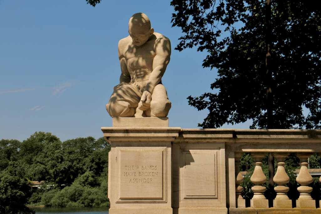 A sculpted figure is hunched over, looking downward.