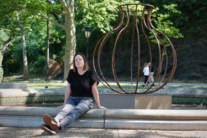 Susan Myers sits down on a step in front of a sculpture.