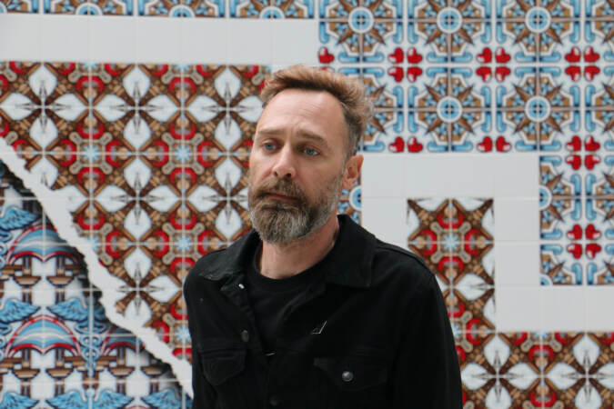 Portuguese visual artist Diogo Machado stands before his mural, ''CRADLE,'' commissioned for Jefferson Plaza in collaboration with Mural Arts Philadelphia. (Emma Lee/WHYY)
