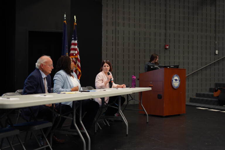 Three people sitting at a table on a stage addressing a crowd.
