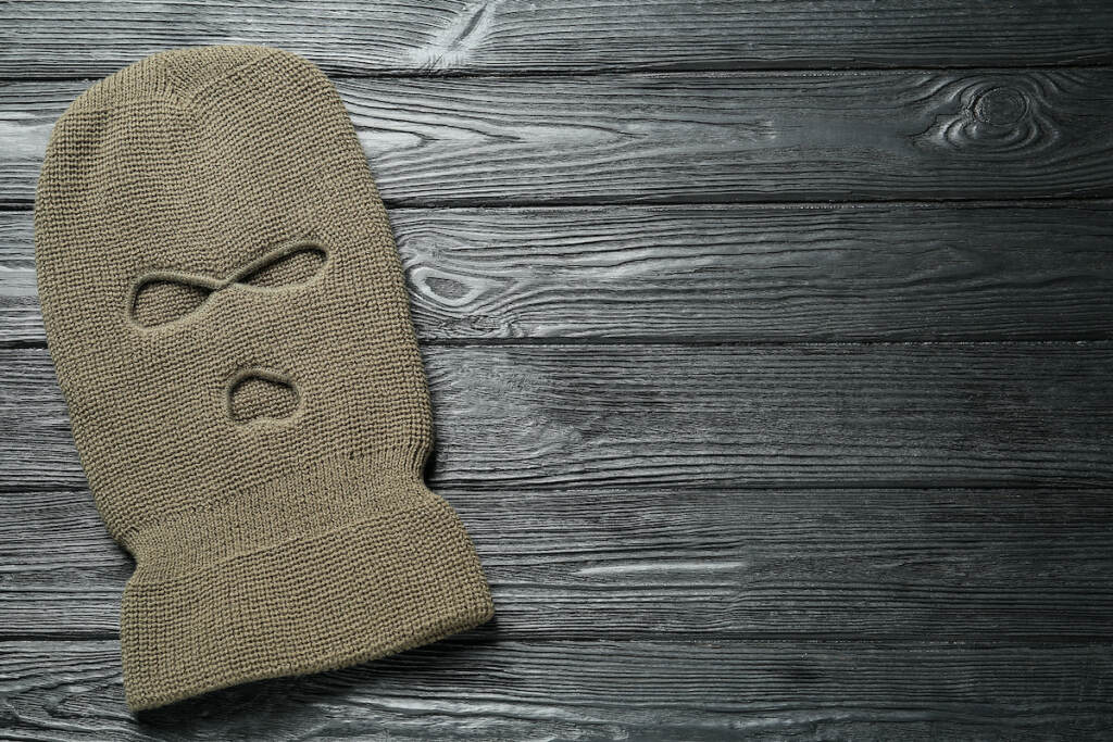 Beige Knitted Balaclava On Black Wooden Table, Top View. Space For Text Beige knitted balaclava on black wooden table