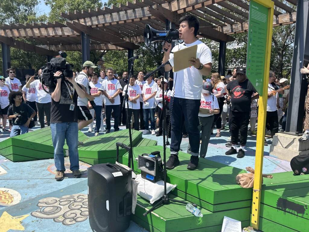 Wei Chen speaks into a megaphone in front of a crowd and members of the media.