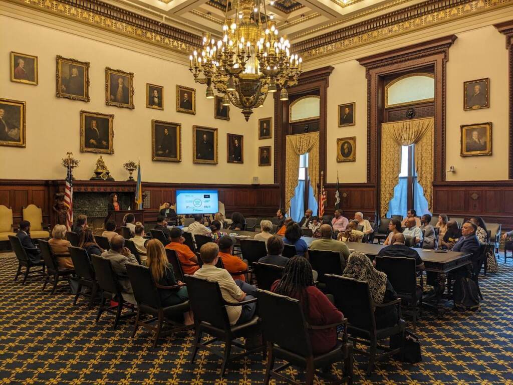 community-grants-review-1 People sit in rows of chairs in a room at Philadelphia's City Hall.