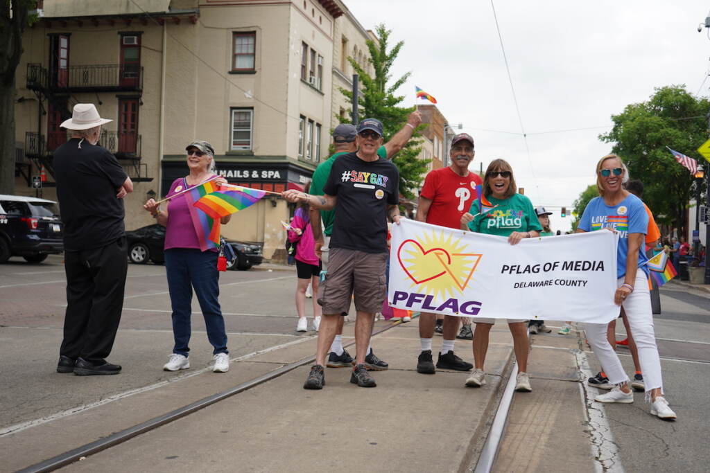 People hold a sign that reads "PFLAG" while holding Pride flags.