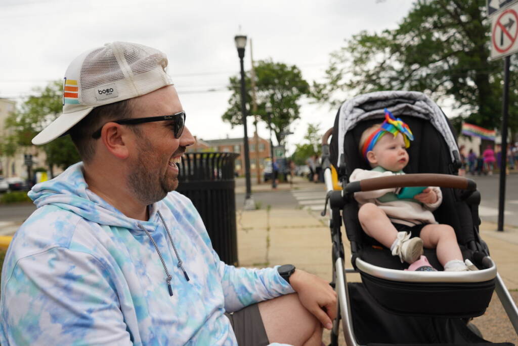 Nick Leister smiles as he sits next to his daughter who is seated in a stroller.