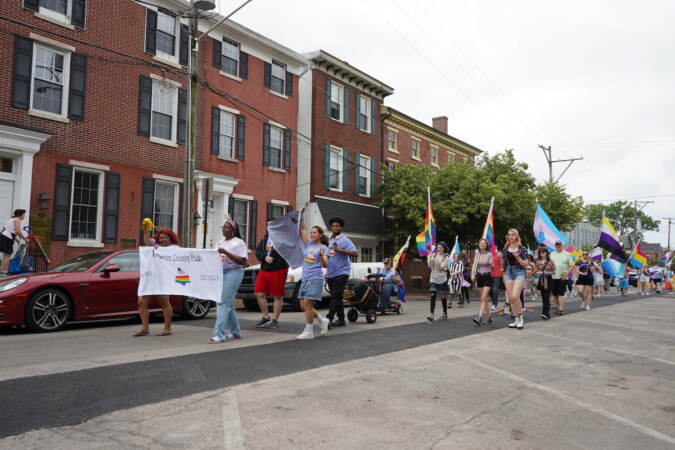People participating in the Pride Parade walk down a street carrying Pride flags and signs.