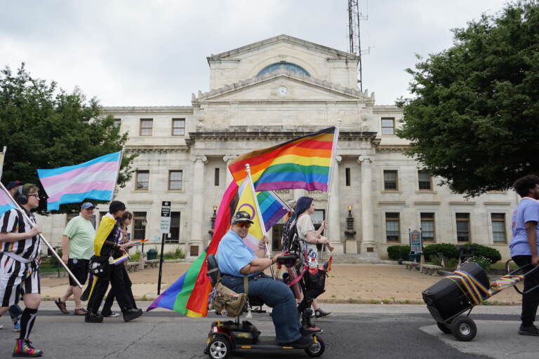 Pride participants pass in front of the Delaware County Courthouse, holding Pride flags.