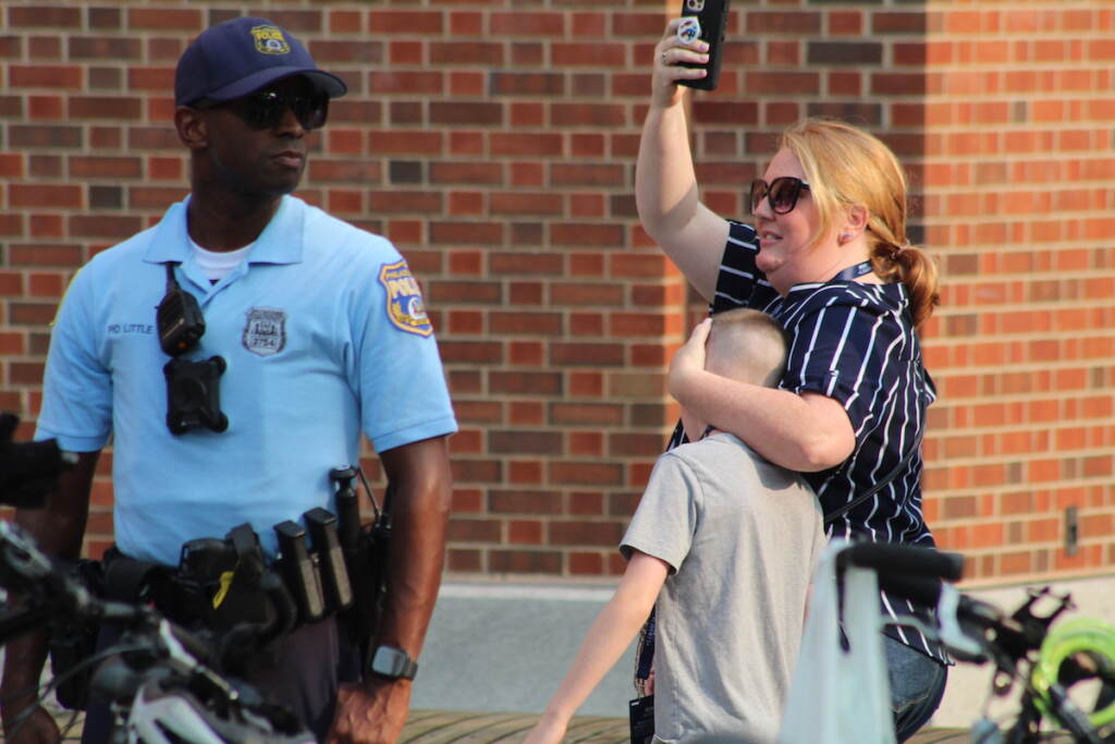 moms-4-liberty-protest-philly-12 A person covers up a child's face as they walk forward. Next to them a police officer looks on.