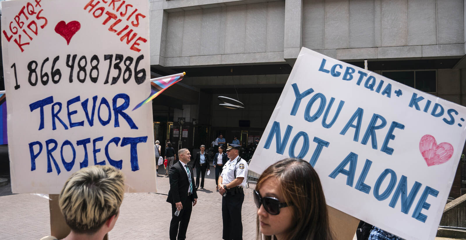 Protest signs outside the Moms for Liberty Summit say ''LGBTQIA+ kids: You are not alone,'' and list the crisis hotline for LGBTQ+ youth, the Trevor Project, at 1-866-488-7386