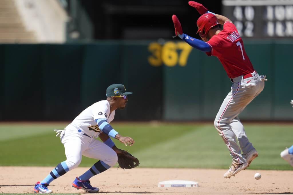 Philadelphia Phillies' Trea Turner, right, jumps over the ball next to Oakland Athletics second baseman Tony Kemp during the eighth inning of a baseball game in Oakland, Calif., Sunday, June 18, 2023. Turner advanced safely to second base after Phillies' Alec Bohm walked on the play