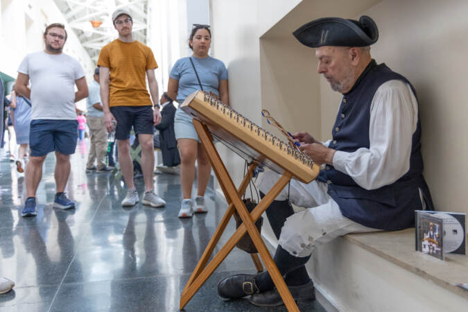 John Lionarons plays a hammered dulcimer as people look on.