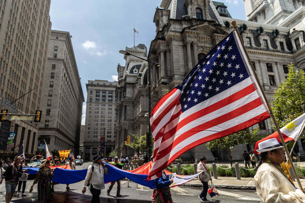 07 03 2023 k paynter fourth of july in philadelphia 2023-8 People carry the U.S. flag as they walk by City Hall in the Fourth of July parade.