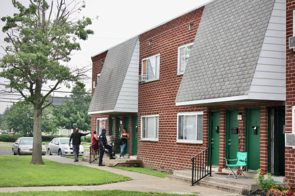 2023 07 19-k burns-camden nj- all american gardens apartments exterior 2 Health inspectors and residents stand outside of a brick apartment building.