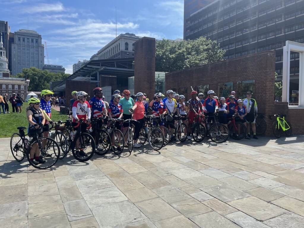 Cyclists pose for a photo in front of Independence Mall on a sunny day.
