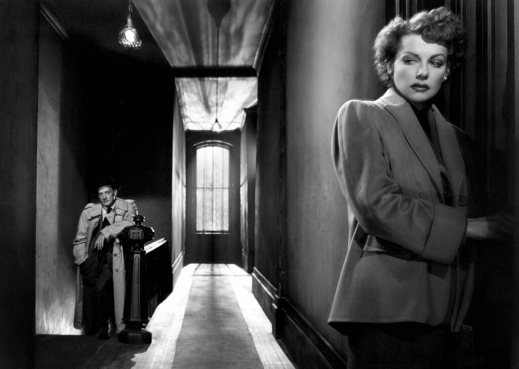 Ann Sheridan opens a door in a black-and-white film still as a man looks on in the background.