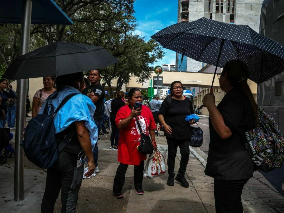 People stand under umbrellas while waiting for a bus during a heatwave in Miami, Florida