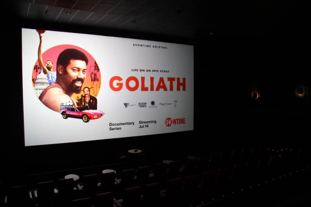 A screen shows the words Goliath with a picture of Wilt Chamberlain