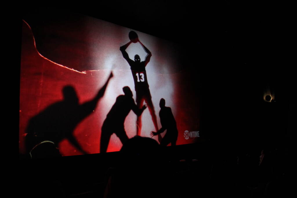 A screens hows basketball players playing. One figure, silhouetted, wears the number 13.