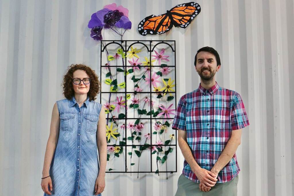 Textile artist Julie ‘’Juicebox’’ Woodard and Eric’’the Puzzler’’ Dale pose for a photo in front of an artwork.