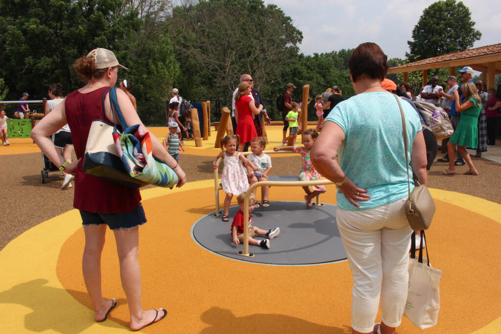 Children play on a carousel as their caregivers look on.