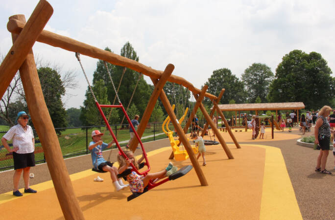 Kids play on swings at a park as their caregivers look on.