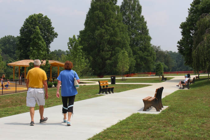People stroll down a walkway lined with benches, grass, and trees.