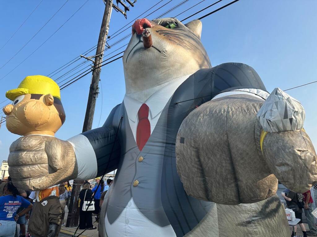 A giant inflatable cartoon cat with a cigar in its mouth is visible.