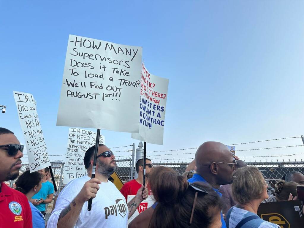 UPS workers and union members hold up signs as they stand together.