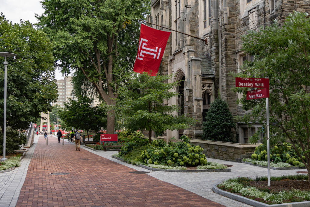 Temple University’s campus in Philadelphia, Pa. (Kimberly Paynter/WHYY) A brick walkway and stone building with a Temple logo flag flying.