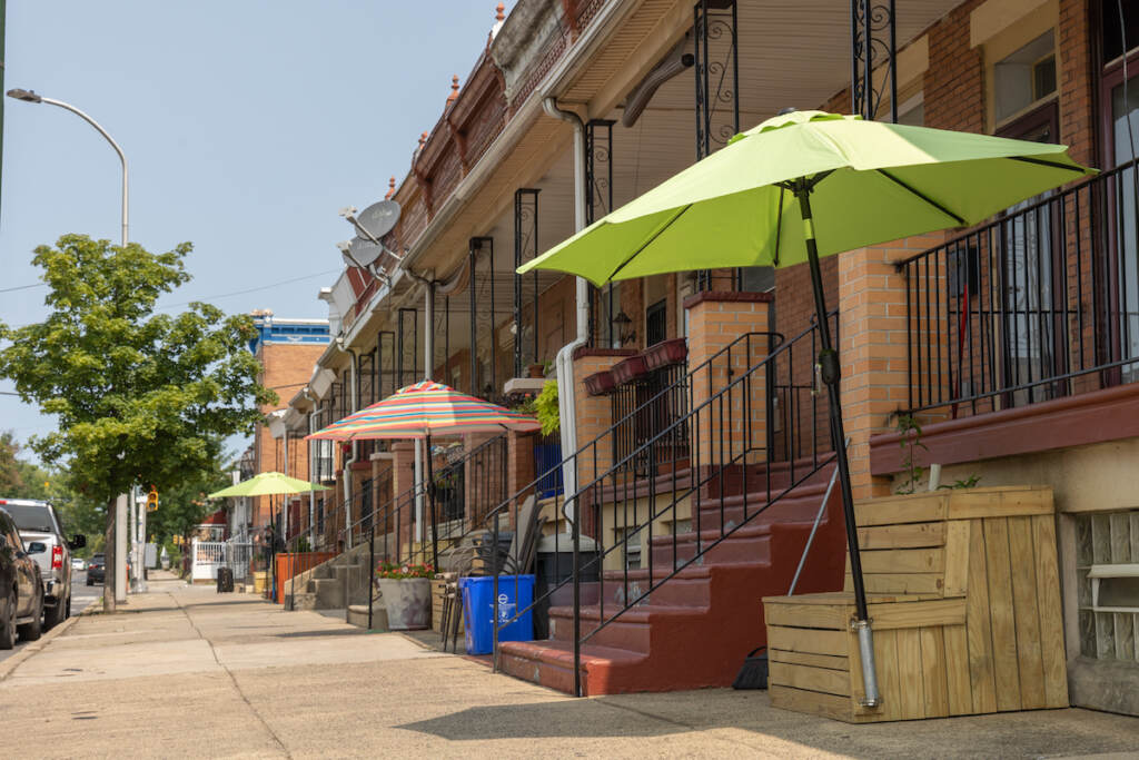 A planter bench with an umbrella overhead sits next to a house in a row of rowhomes.