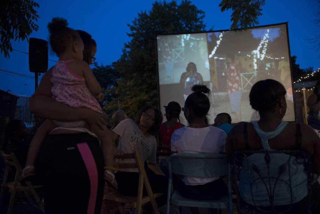People watch a movie on a projector screen outdoors.