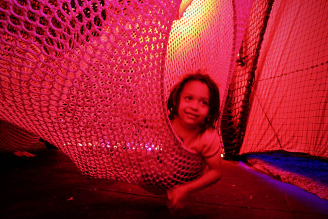 Dash Curley looks out from a hammock in a pink light filled room.