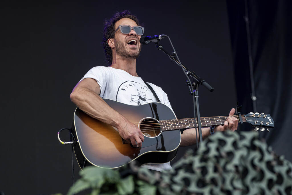 Amos Lee performs at Railbird Music Festival on Sunday, June 4, 2023, at The Infield at Red Mile in Lexington. He is holding a guitar in his hands and sings into a microphone.