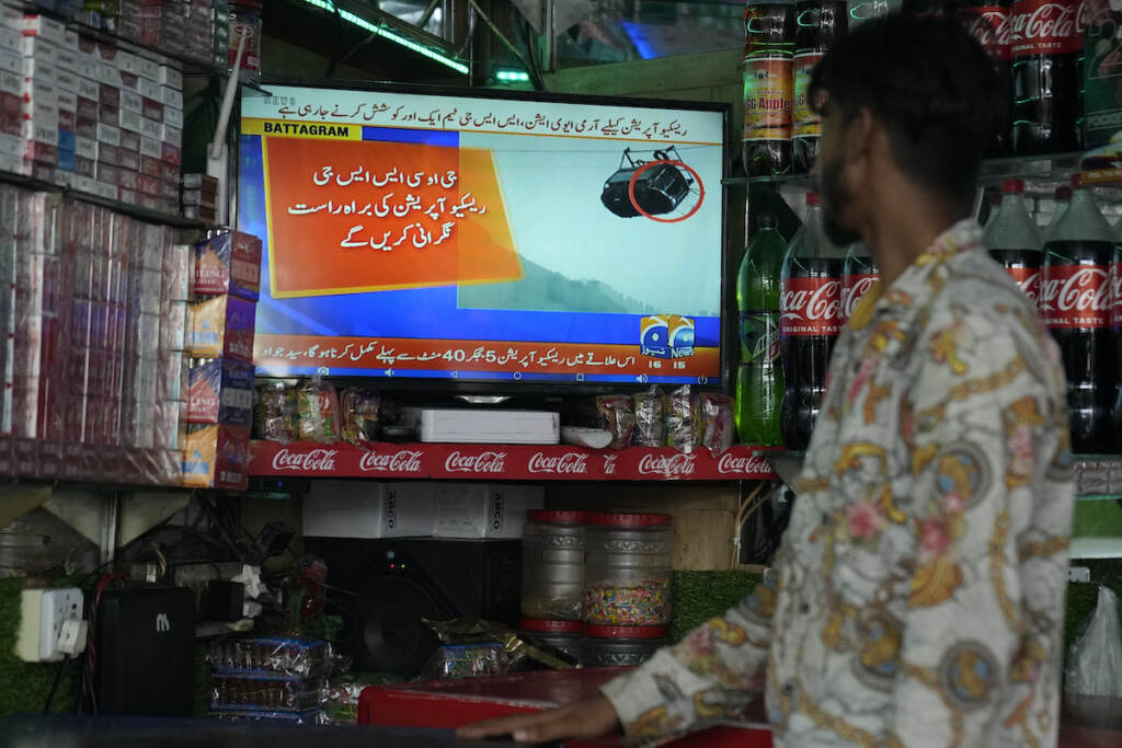 Pakistan Children Trapped A shopkeeper watches a news channel airing news regarding people trapped in a cable car, at his shop in Lahore, Pakistan, Tuesday, Aug. 22, 2023. A cable car carrying six children and two adults dangled hundreds of meters (feet) above the ground in a remote part of Pakistan after it broke on Tuesday, trapping the occupants for hours before rescuers arrived in helicopters to try to free them.