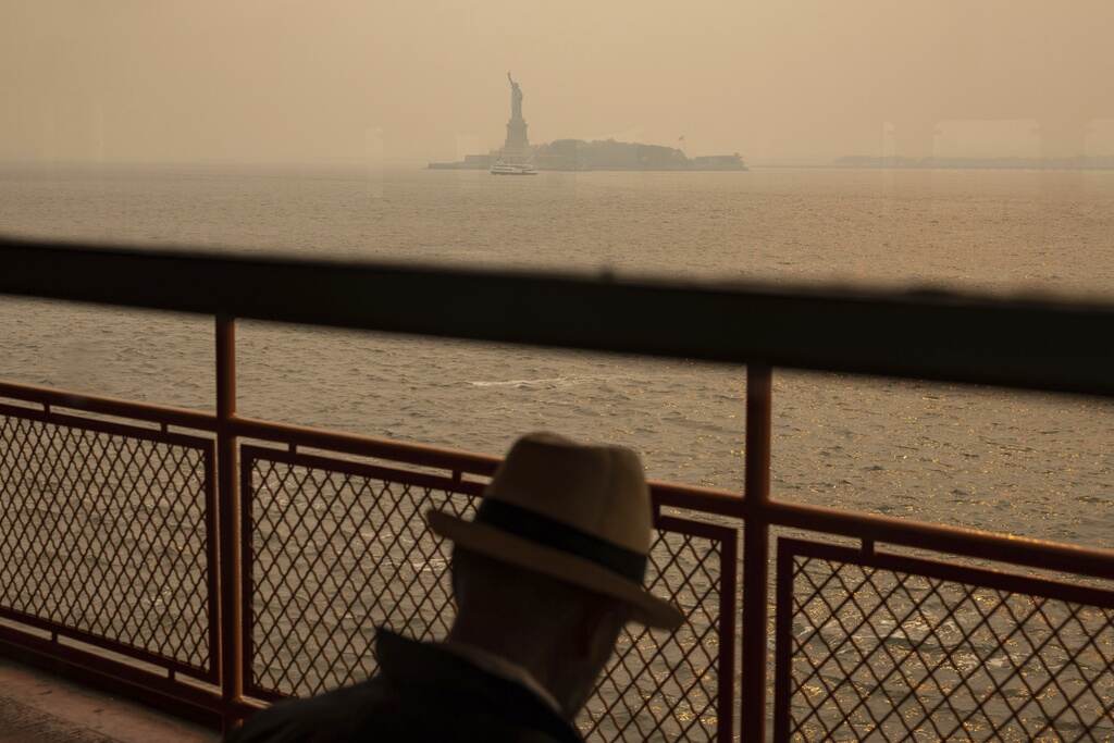 The Statue of Liberty is visible in the distance, shrouded in a smoky haze. A person is visible in the foreground, facing away from the camera.