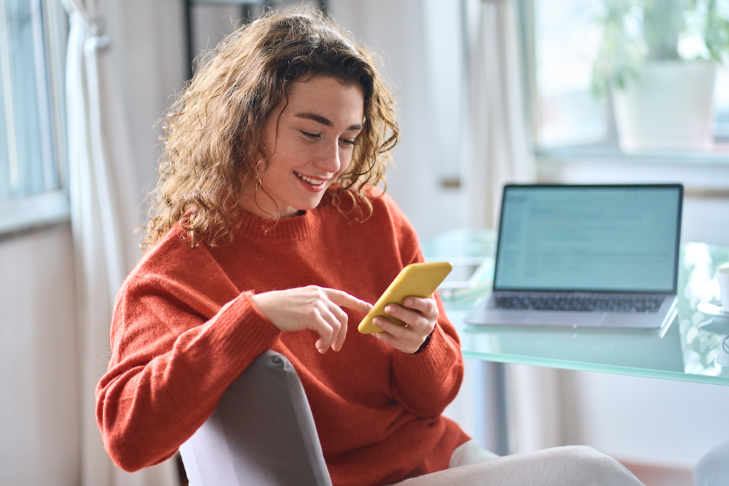 A woman is happily using her cell phone while working remotely at home (Big Stock/ViShark).