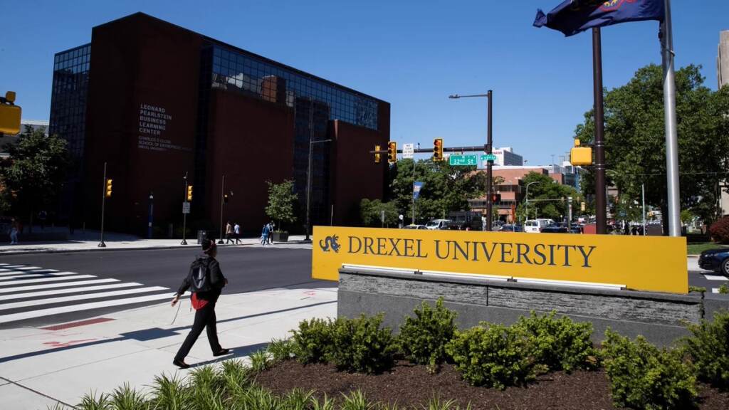 drexel A person walks by a sign reading Drexel University.