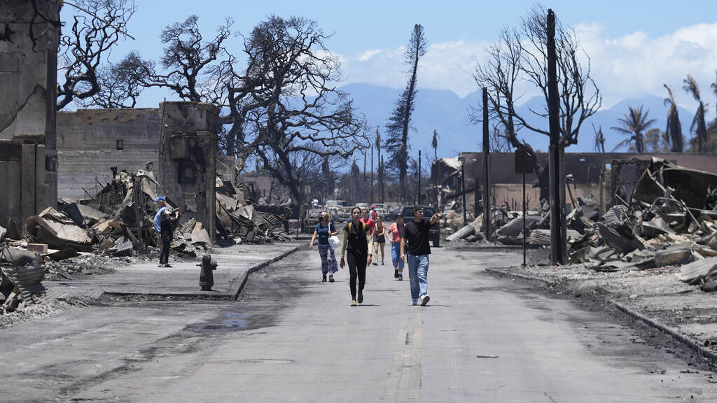 Hawaii Fires People walk down a road with damaged and burned wreckage visible on either side