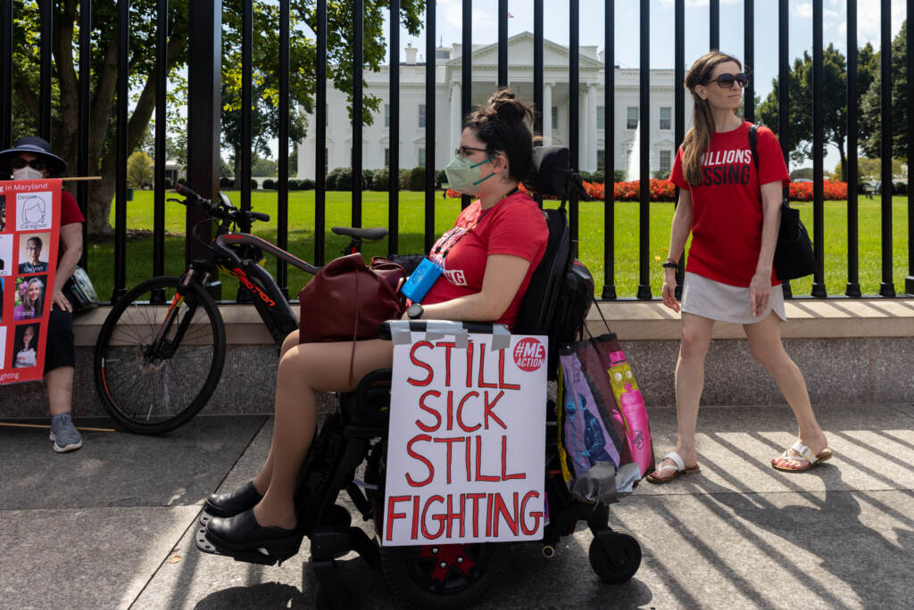 A woman in a wheelchair displays a sign that reads 