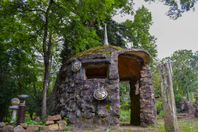 A stone hut structure stands amid trees.