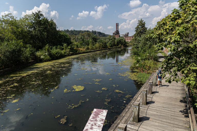A person walks along the Schuylkill River Trail near the Manayunk Canal, as seen from above.