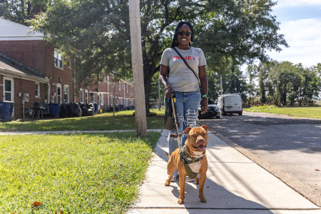 Southbridge neighborhood resident Melodi Robinson walks her dog Sesame on a sidewalk, smiling.