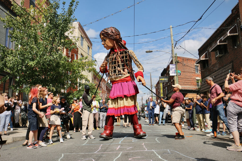Little Amal, a 12-foot-tall puppet, plays hopscotch with children and community members on Passyunk Ave.