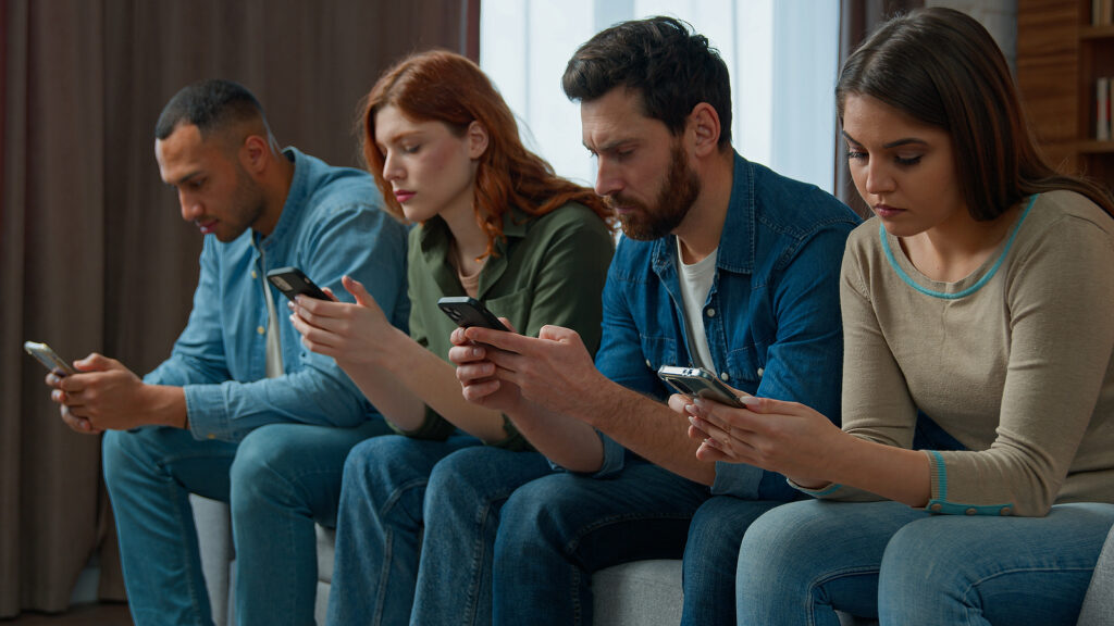 Millennial 30s diverse people sit in line on sofa holding smartphone ignoring friends chatting online in messenger mobile phone addicted women men internet overuse problem modern wireless tech usage